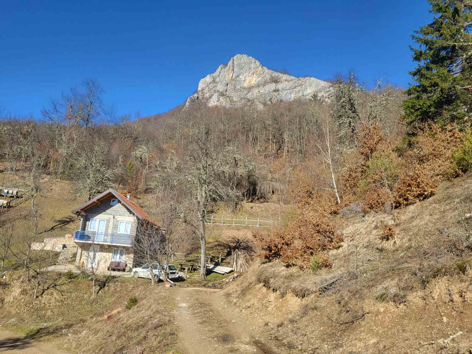 mountains visible in the distance in a samll house and a dirt road in front on a sunny day